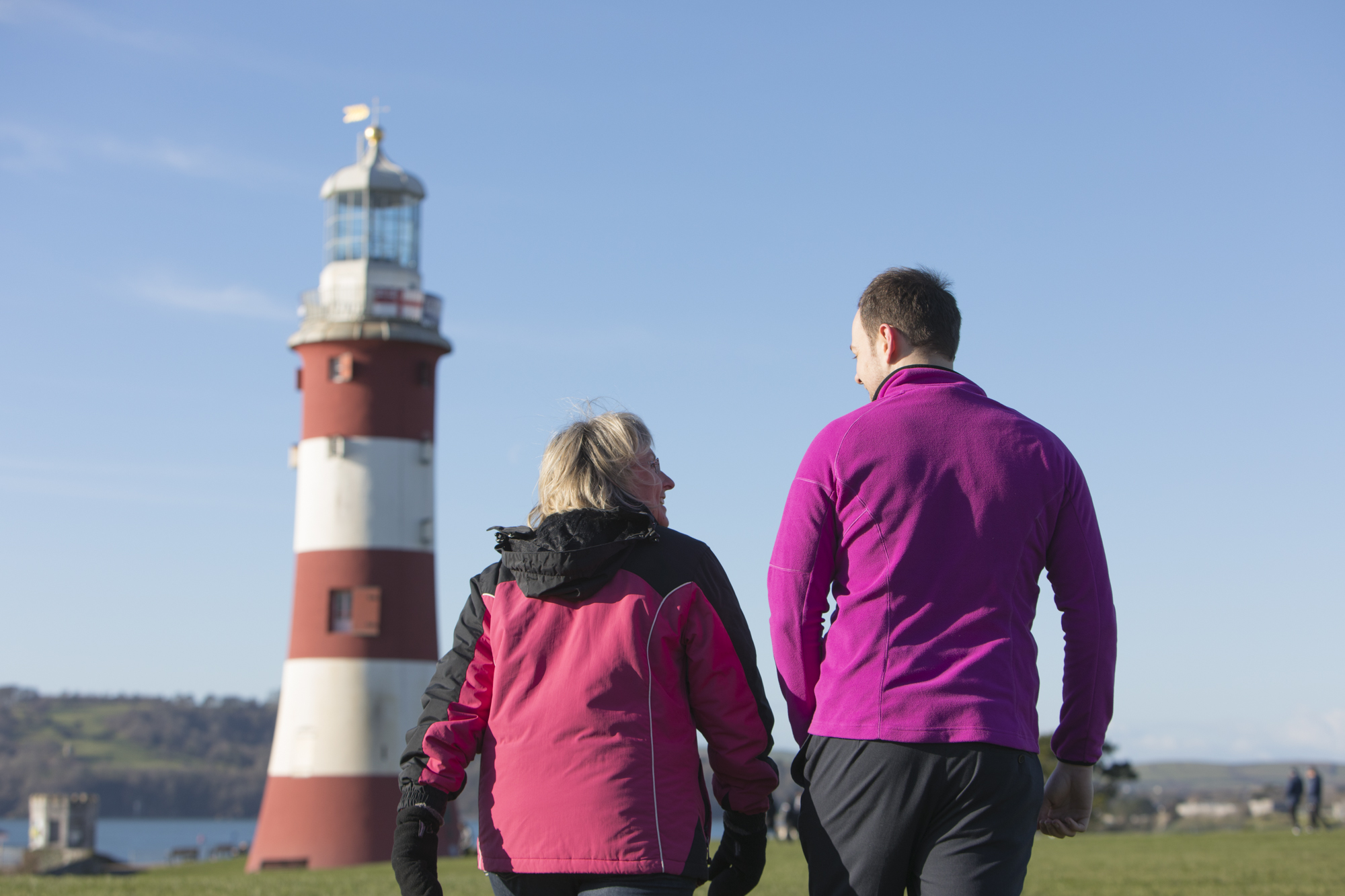 two people walking along with lighthouse tower in the background