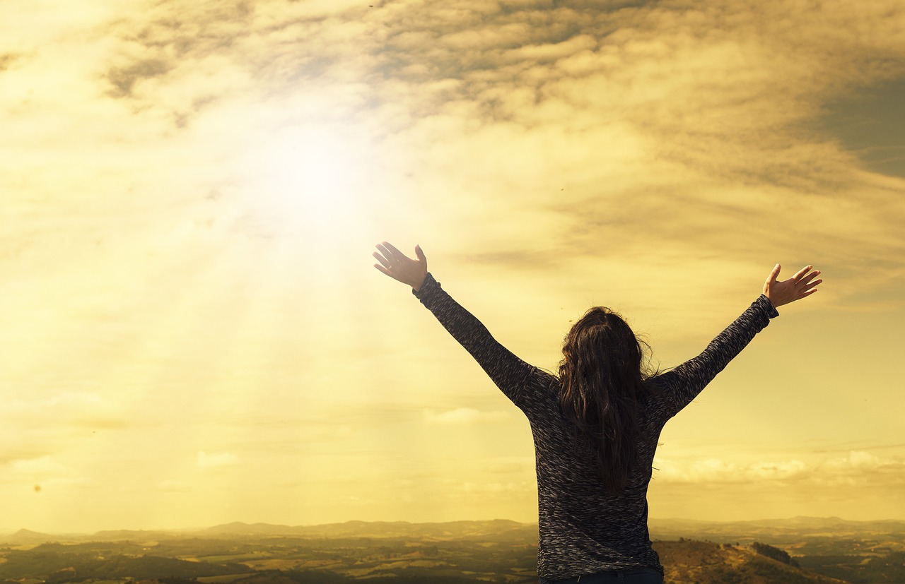 woman standing with arms out stretch in front of the sunshine